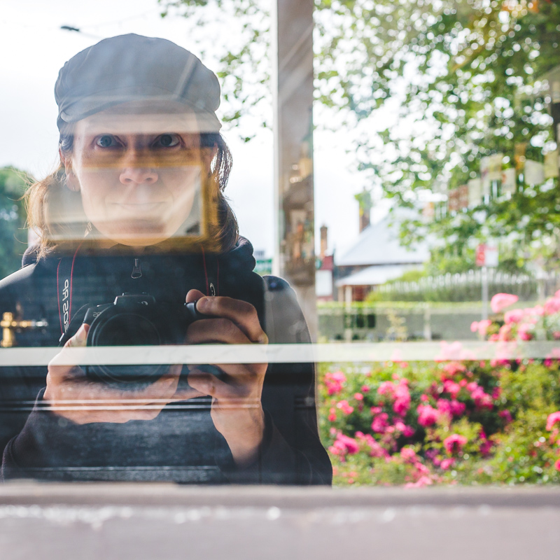 A woman holding a camera reflected in a window.