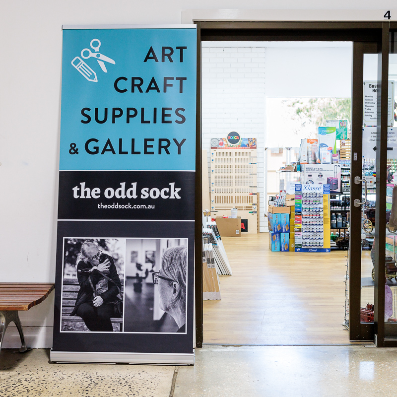 A tall vinyl banner on a stand outside a shop's entrance.