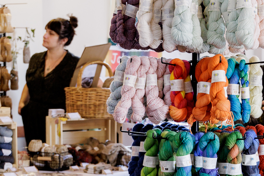 A person standing behind a yarn stall at a fibre festival